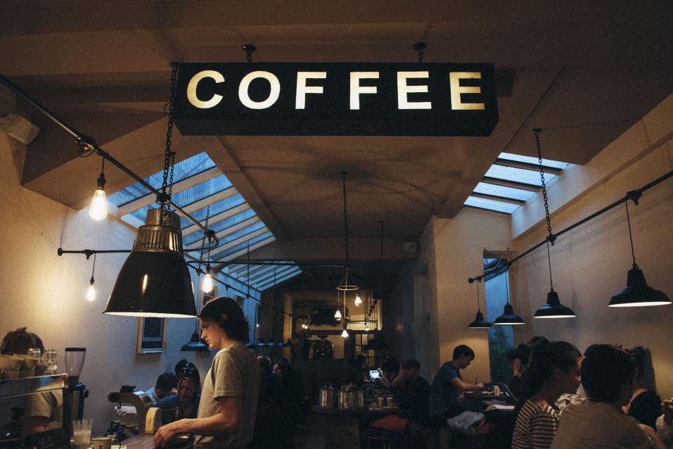 Baristas and customers in a busy coffee shop under a big COFFEE sign