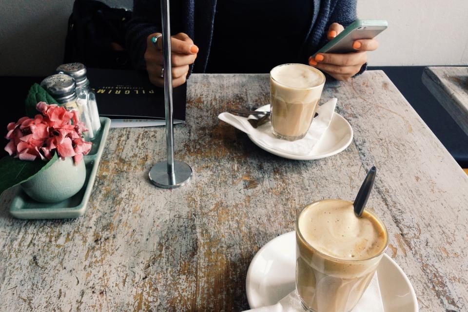 Two coffees on a café table while a customer checks their phone