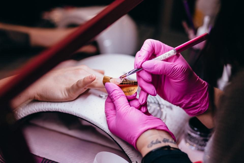 A nail technician in pink gloves shaping a client’s nails