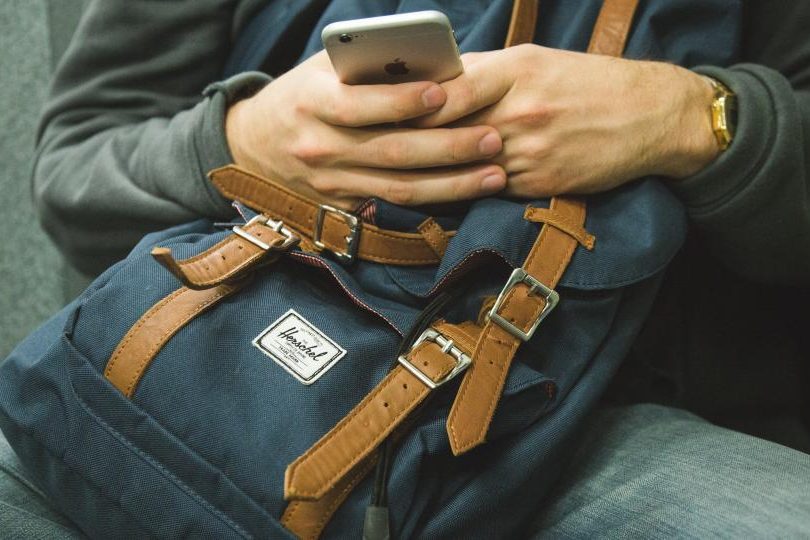 A person texting on their phone while holding a coffee